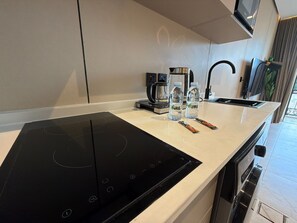 Eine moderne Küche mit einer schwarzen Induktionskochplatte, einer Kaffeemaschine und zwei Wasserflaschen auf der Arbeitsfläche.