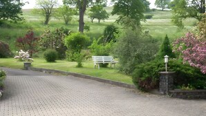 A paved driveway leading to a bench in a landscaped area with trees and shrubs. - Apartment “Haus Am Fischbach” with Shared Terrace, Garden, and Wi-Fi (Waltershausen)