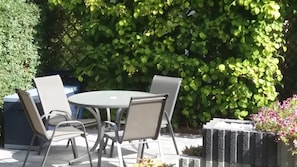 Ulkoterassi, jossa on pyöreä pöytä ja neljä tuolia, ja sen ympärillä on vehreää kasvillisuutta.
