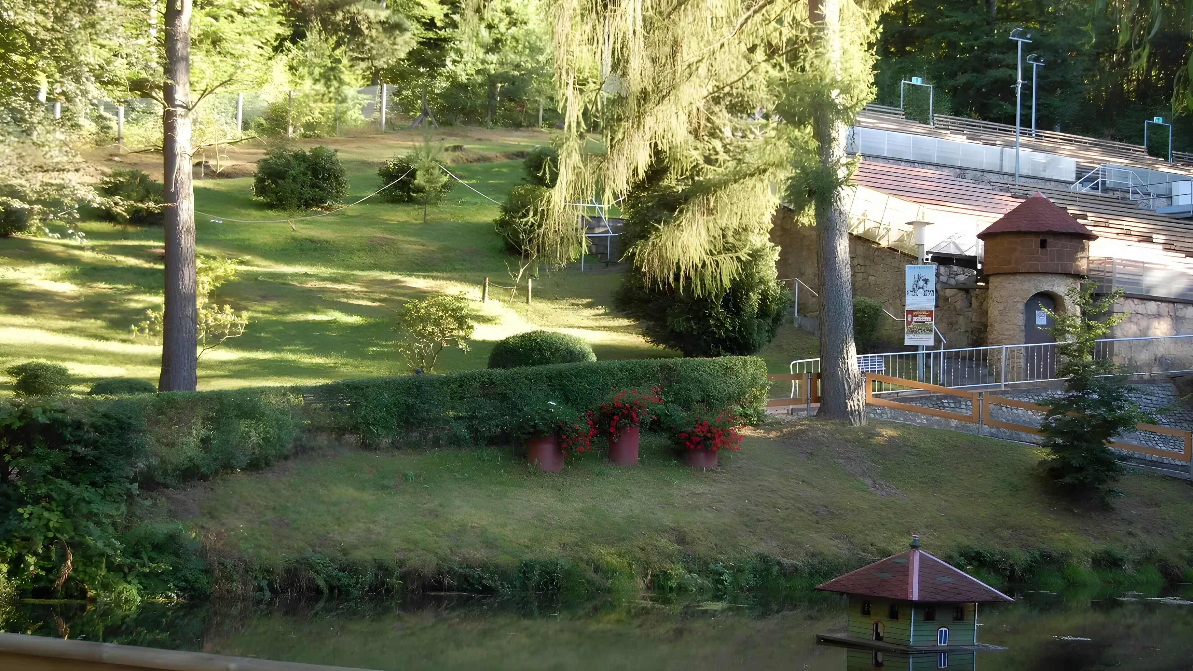 A park with a pond, a gazebo, and a building with a red roof.