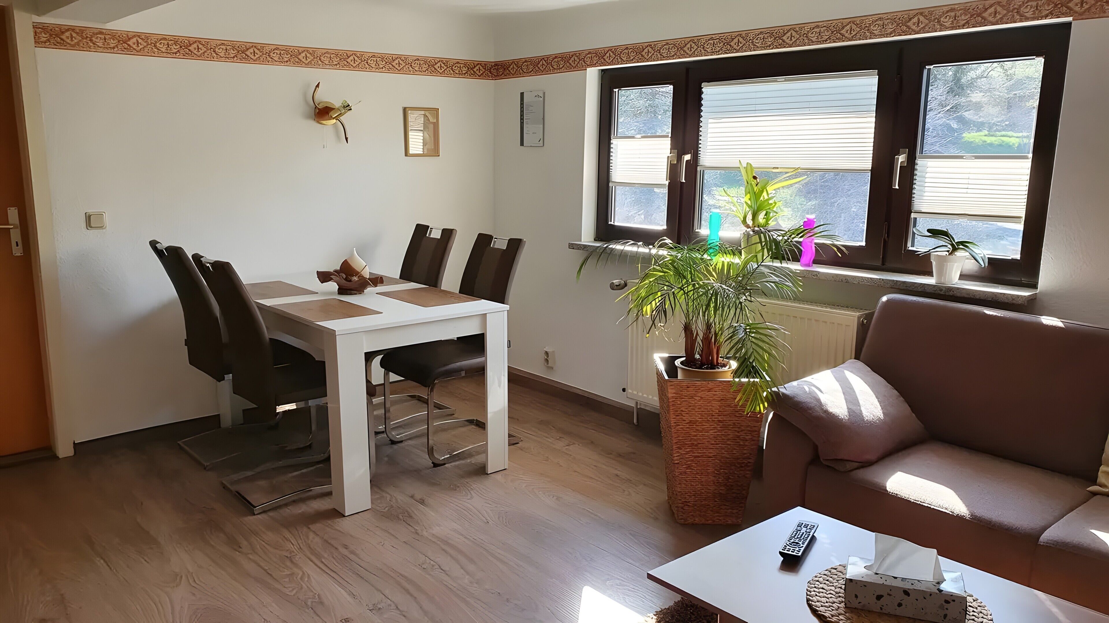A dining area with a white table and chairs, a potted plant, a remote control, and a couch.