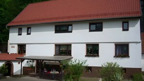 A two-story building with a red-tiled roof, multiple windows, and a covered porch area. - Apartment “Haus Am Fischbach” with Shared Terrace, Garden, and Wi-Fi (Waltershausen)