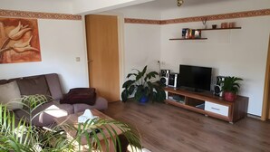 A living room with a sofa, TV, speakers, and a plant. - Apartment “Haus Am Fischbach” with Shared Terrace, Garden, and Wi-Fi (Waltershausen)