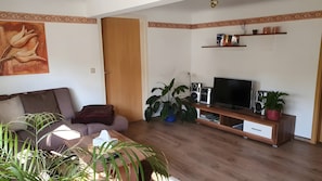 A living room with a sofa, TV, speakers, and a plant.