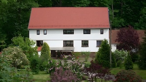 A two-story building with a red-tiled roof, multiple windows, and a covered entrance. - Apartment “Haus Am Fischbach” with Shared Terrace, Garden, and Wi-Fi (Waltershausen)