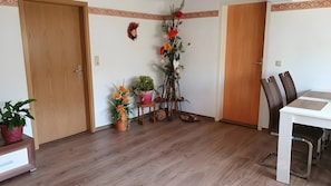 A dining area with a wooden table and chairs, a potted plant, and a decorative plant stand with flowers. - Apartment “Haus Am Fischbach” with Shared Terrace, Garden, and Wi-Fi (Waltershausen)