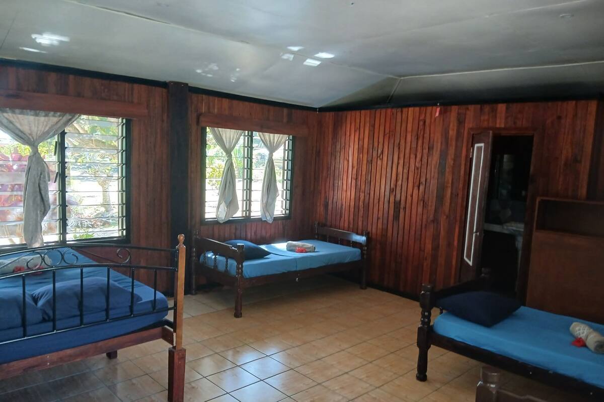 Una habitación con dos camas de madera, una ventana con cortinas y un suelo de baldosas.