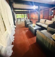 Un espacio de estar al aire libre con techo, mobiliario de mimbre, una mesa y vistas del exterior.