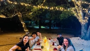 Un área de comedor al aire libre con una mesa lista para una comida, rodeada de árboles y luces colgantes.