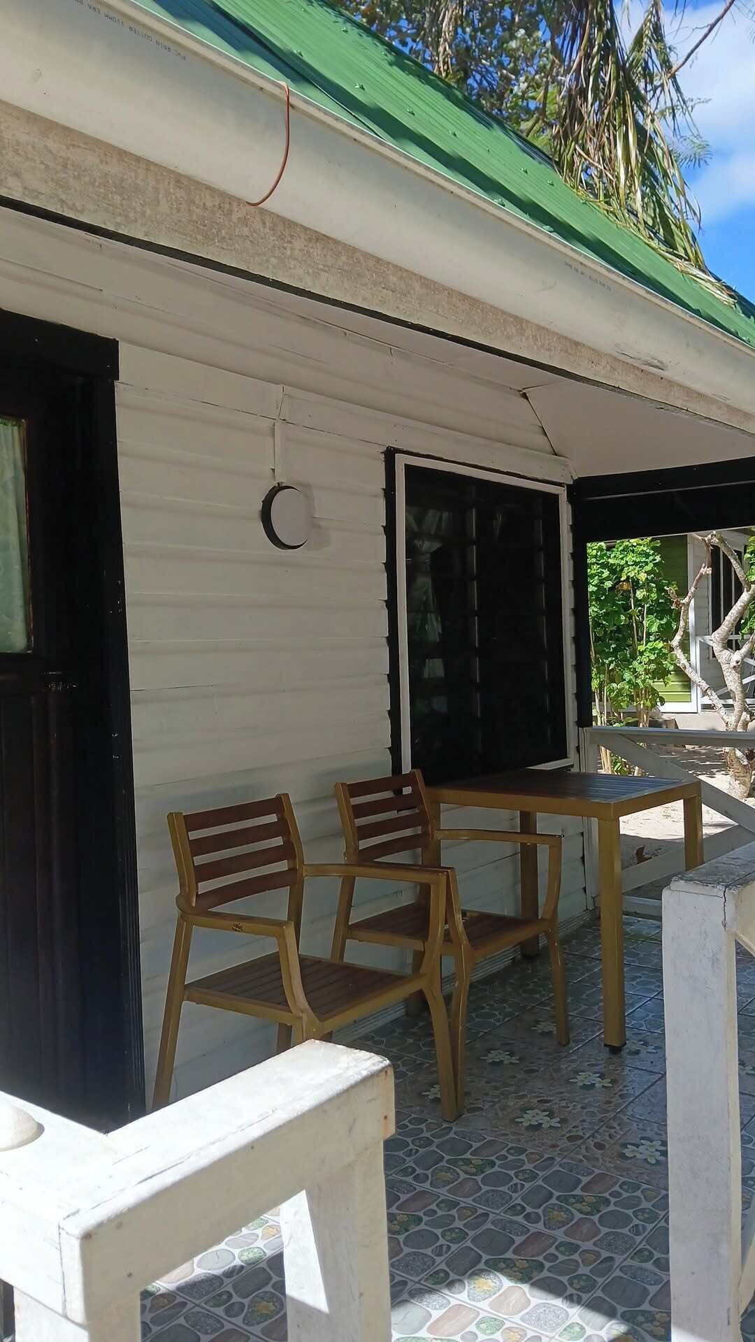 A covered outdoor seating area with a table and chairs, a window, and a door.