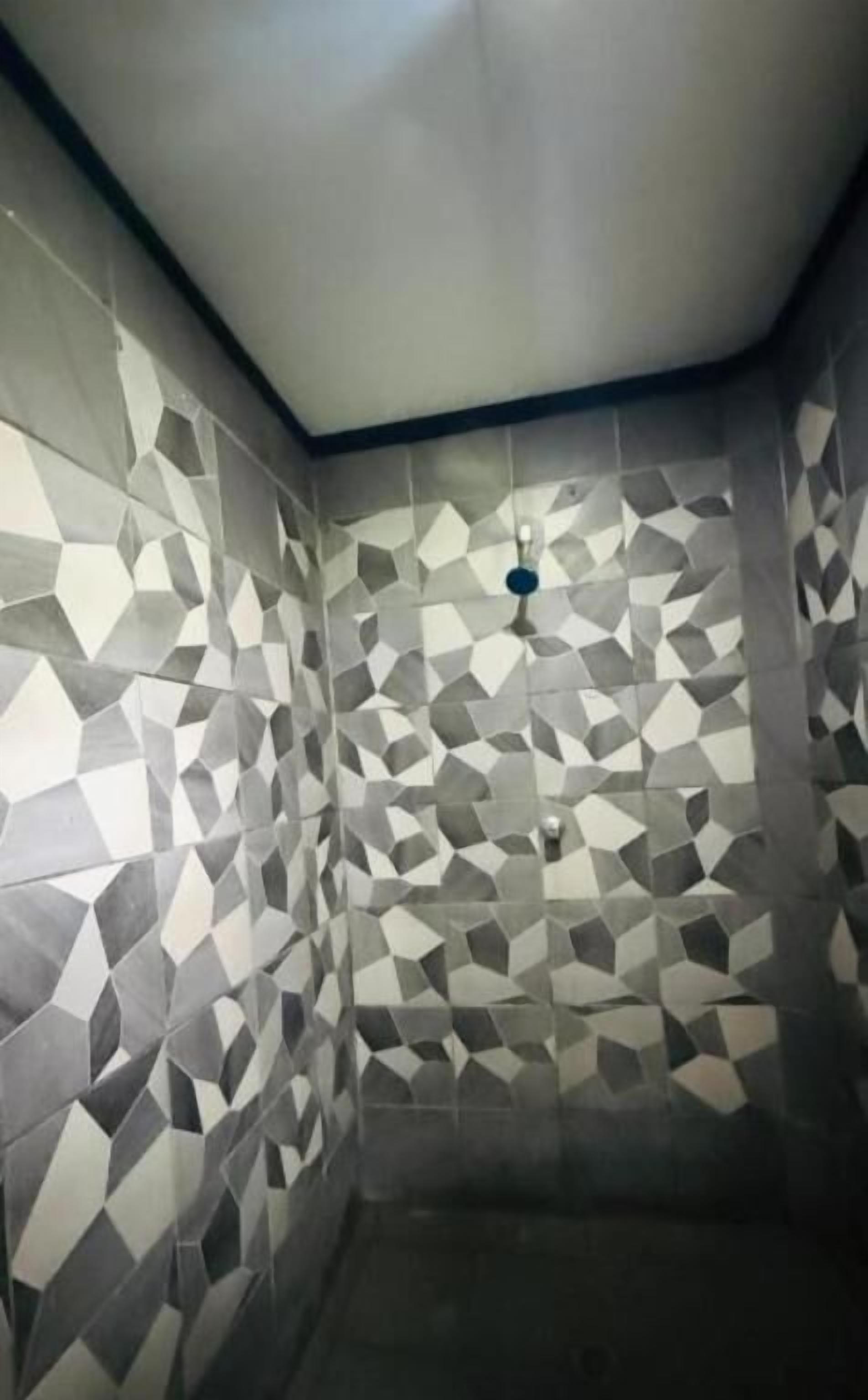Un baño con baldosas de diseño geométrico, un ventilador de techo y un desagüe de ducha visible.