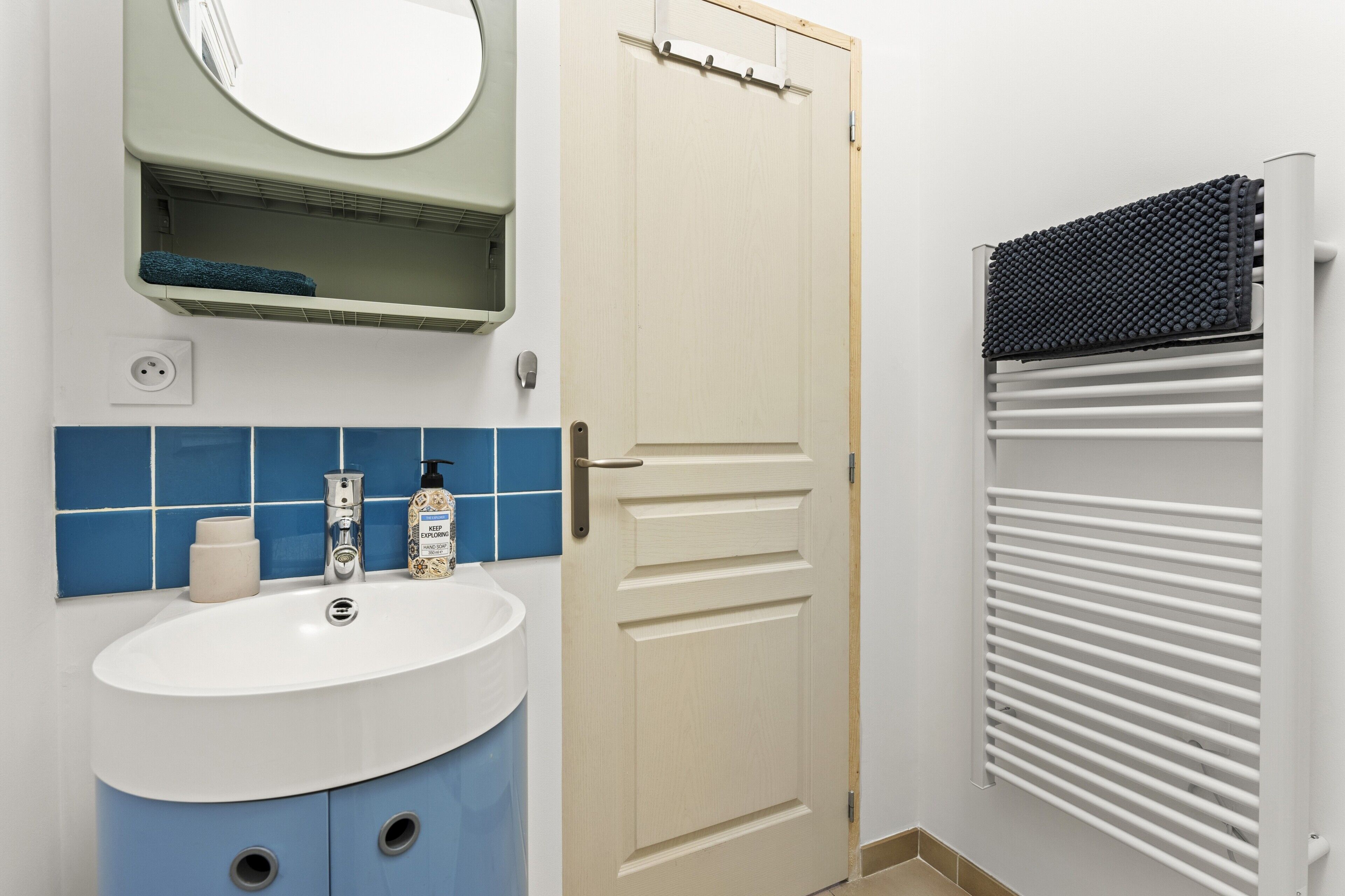 A bathroom with a sink, mirror, towel rack, and radiator.