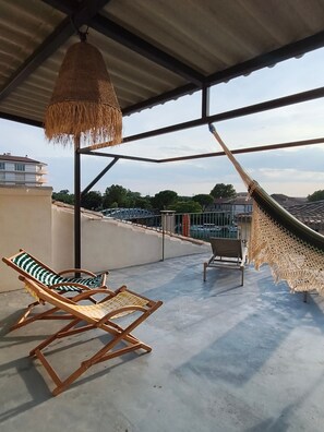 A covered outdoor area with a hammock, two lounge chairs, and a view of buildings in the distance. - Spacious and Cozy Apartment with Terrace and Bike Storage in Central Beaucaire (Beaucaire)