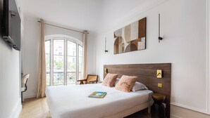 Et hotelværelse med en stor seng, et fladskærms-tv, et maleri og udsigt fra vinduet.