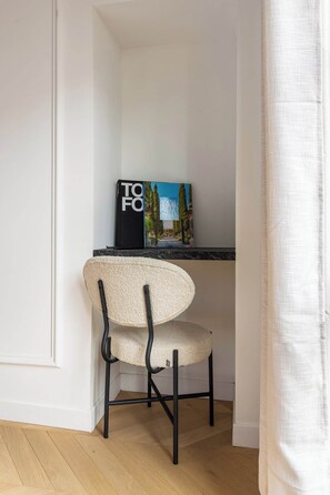 A corner room with a white wall, a wooden floor, a black chair with a textured seat, a black book titled 'TO FO,' and a painting above the chair. - Luxurious apartment - 6 people - 11/12th floor (Paris)