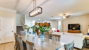 Amplia sala de estar con mesa de comedor, sillas, sofá, televisor y una escalera que sube a otro nivel.