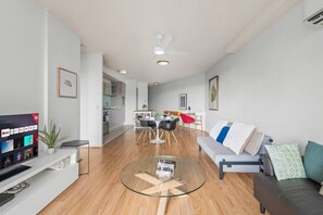 A modern living room with a glass coffee table, a sofa, a TV, and a dining area with a red chair. - Modern Inner-City Stay in Valley|Heart of Brisbane (Fortitude Valley)