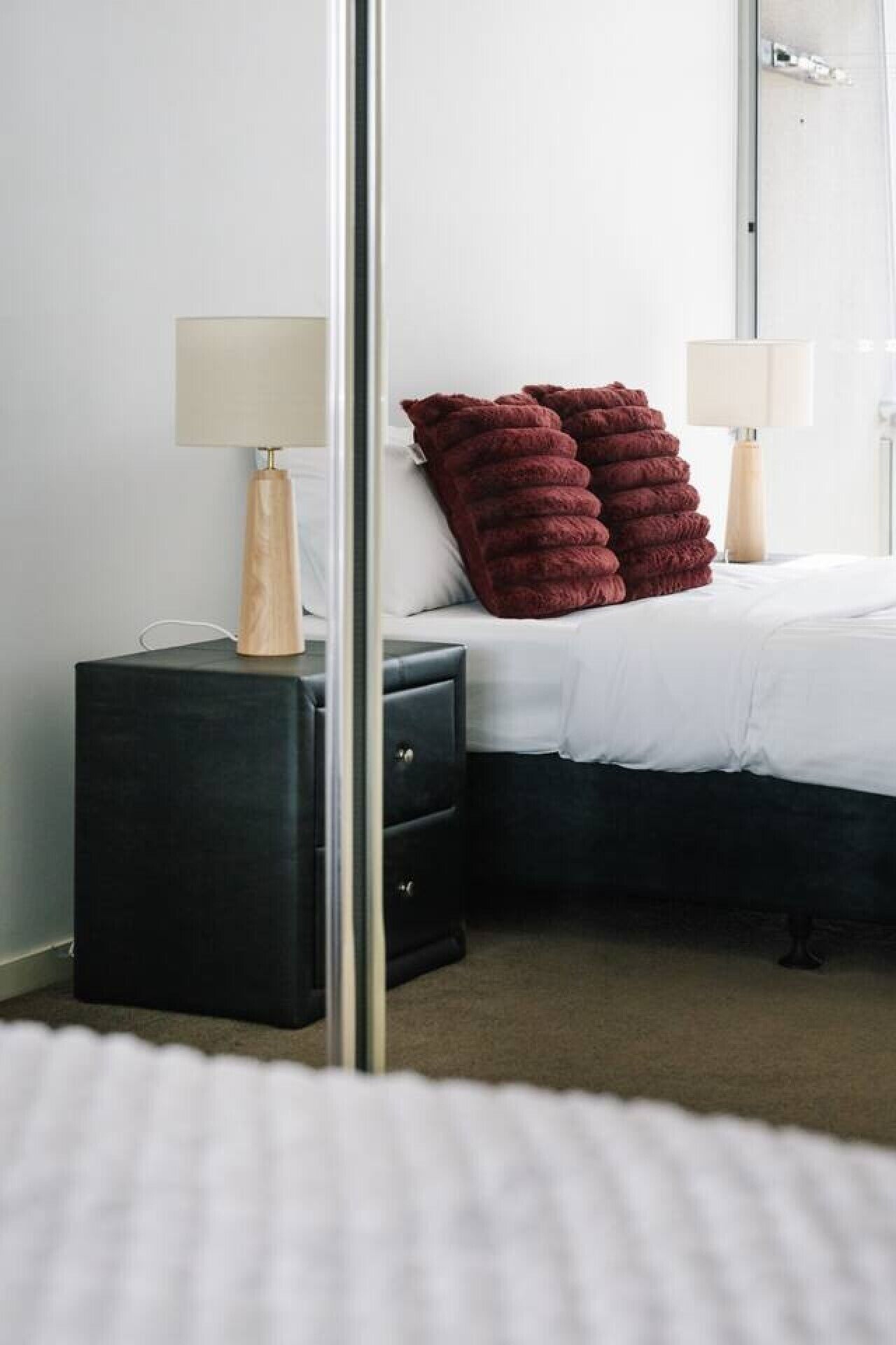 Un dormitorio con cama, mesita de noche, lámpara y espejo.