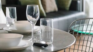 A dining table with plates, glasses, and cutlery, a chair, and a sofa in the background. - Modern Inner-City Stay in Valley|Heart of Brisbane (Fortitude Valley)
