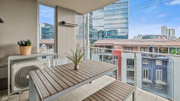 A balcony with a table and chairs, a potted plant, and a wall-mounted fan. - Modern Inner-City Stay in Valley|Heart of Brisbane (Fortitude Valley)