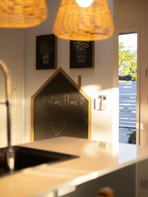 A reception area with a chalkboard sign reading 'Welcome Home,' a potted plant, and a door leading outside. - Stylish Family Home w/ A/C, 5 mins to Westfield (Upper Mount Gravatt)
