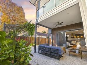 Una casa moderna con un patio que cuenta con un sofá, sillas, un ventilador de techo y vistas al jardín trasero.