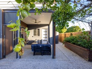 A covered outdoor patio with a seating area, a pergola with hanging fruit, and a wooden fence in the background. - Stylish Family Home w/ A/C, 5 mins to Westfield (Upper Mount Gravatt)