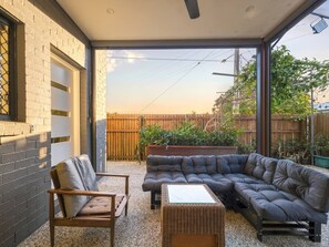 Eine überdachte Terrasse mit einer Eckcouch, einem Sessel und einem kleinen Tisch.