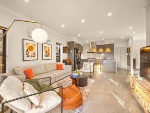 A modern living room with a sofa, coffee table, and a dining area with pendant lights. - Stylish Family Home w/ A/C, 5 mins to Westfield (Upper Mount Gravatt)