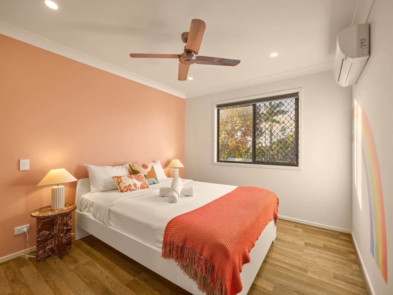 A bedroom with a bed, a ceiling fan, a window with a view, a nightstand, and a lamp.