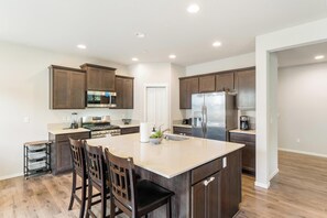A modern kitchen with dark wood cabinets, stainless steel appliances, and a large island with bar stools. - Serene 4-bedroom house in Lake Stevens perfect for relaxing stays (Lake Stevens)