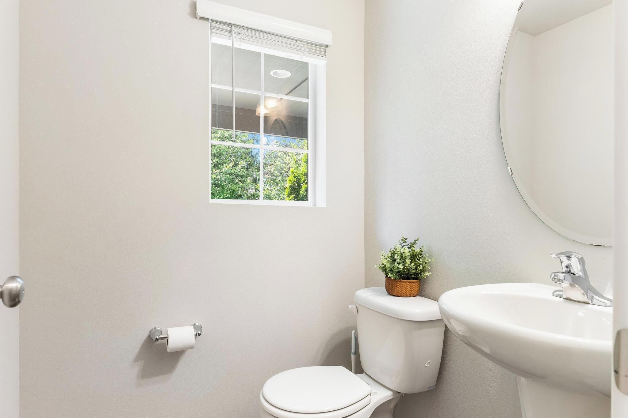 Ein Badezimmer mit Toilette, Waschbecken, Fenster mit Blick auf Grünflächen und einer Tür.