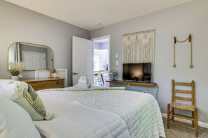 A bedroom with a bed, a wooden chair, a desk with a computer, a mirror, and a wall-mounted macrame piece. - Outdoor Fun! Charming Family Home in Tobyhanna (Tobyhanna)