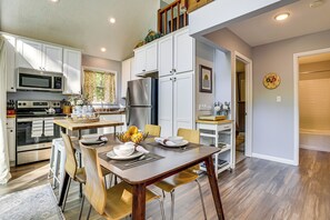 Une cuisine moderne avec des meubles blancs, des appareils en acier inoxydable et un coin repas comprenant une table et des chaises en bois.