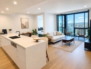 A modern apartment with a kitchen, living area, and large windows offering city views. - 2BR Story Bridge Views | Resort Pool & Parking (Brisbane)