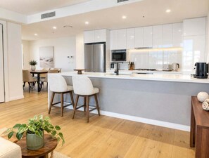 A modern kitchen with white cabinets, stainless steel appliances, and a central island with bar stools. - 2BR Story Bridge Views | Resort Pool & Parking (Brisbane)