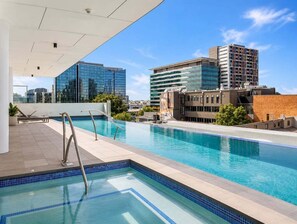 A rooftop swimming pool with a cityscape view, modern buildings, and a clear sky. - 2BR Story Bridge Views | Resort Pool & Parking (Brisbane)