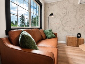 Una habitación con un sofá de cuero, un mural con un mapa, una lámpara de pie y una mesita de madera.