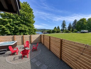 A patio area with a hot tub, red chairs, and a view of a lake and forest.
