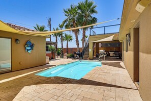 Ein Schwimmbecken mit gefliestem Deck, Palmen und einer überdachten Terrasse.