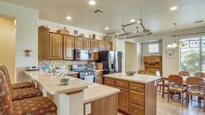 A kitchen with wooden cabinets, a central island, a dining area with chairs, and a large window. - Pool Access! Extended Desert Escape Near St George (Washington)