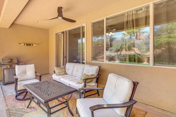 Eine Terrasse mit Deckenventilator, Grill und einer Couch mit Kissen.