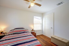 Ein Schlafzimmer mit einem Bett, einem Nachttisch, einer Nachttischlampe, einem Fenster mit Jalousien, einer Tür und einem Deckenventilator.
