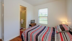 A bedroom with a bed, a television, a window, and a ceiling fan.
