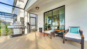 Une terrasse avec un barbecue, un canapé en osier et une porte vitrée donnant sur un balcon.
