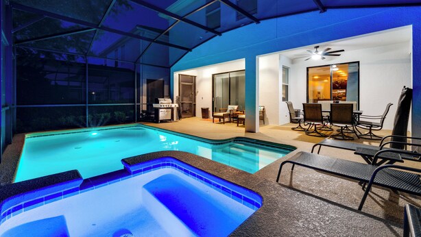 Une piscine entourée de parois en verre, un espace barbecue et un coin repas avec chaises et tables.