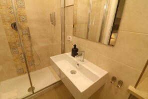 Ein Badezimmer mit einem weißen Waschbecken, einer Handbrause und einer Duschkabine aus Glas.