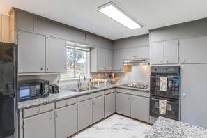 Eine moderne Küche mit grauen Schränken, einem Edelstahl-Kühlschrank, einer Mikrowelle, einem Spülbecken und einem eingebauten Backofen.