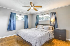 Ein Schlafzimmer mit Bett, Deckenventilator, Nachttisch und einem Fenster mit Vorhängen.
