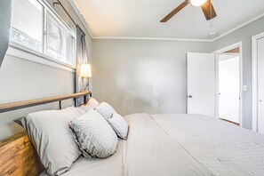 Ein Schlafzimmer mit Bett, Deckenventilator, Fenster mit Vorhängen und einer Tür.